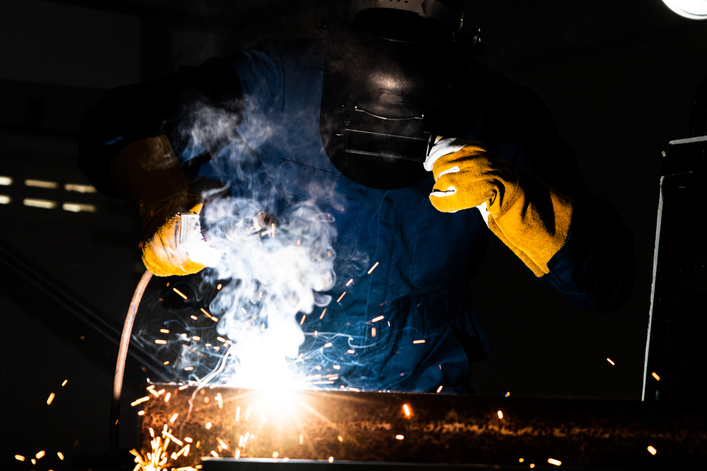 金属焊工与弧焊机一起工作在工厂焊接钢同时佩戴安全设备通过手工技能劳动概念的金属制品制造和建筑维护服务